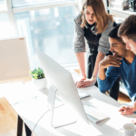 Startup coworkers collaborating at a computer, reviewing cloud infrastructure dashboards to represent Kubernetes adoption for startups.