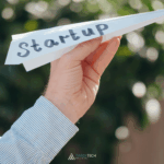 Person launching a paper airplane labeled ‘STARTUP,’ symbolizing scalable growth and the power of CloudOps in helping startups move fast and control cloud costs.